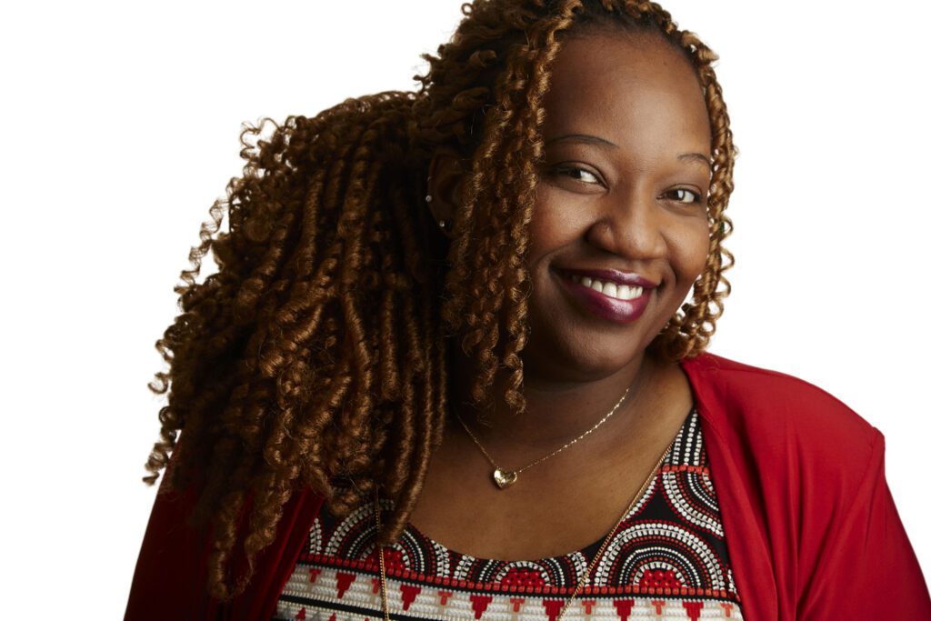 Real estate agent headshot of a smiling woman with long braided hair wearing a red cardigan and patterned top, white background, taken in Kitchener