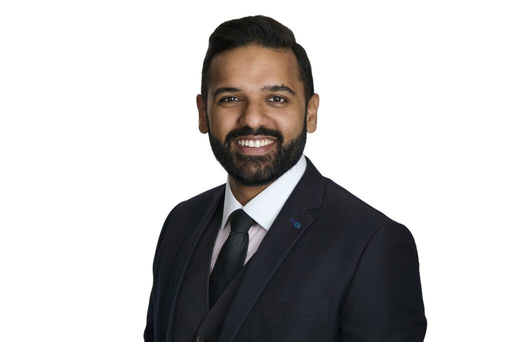 Waterloo business headshot: smiling man in a dark three-piece suit and tie on a white background.